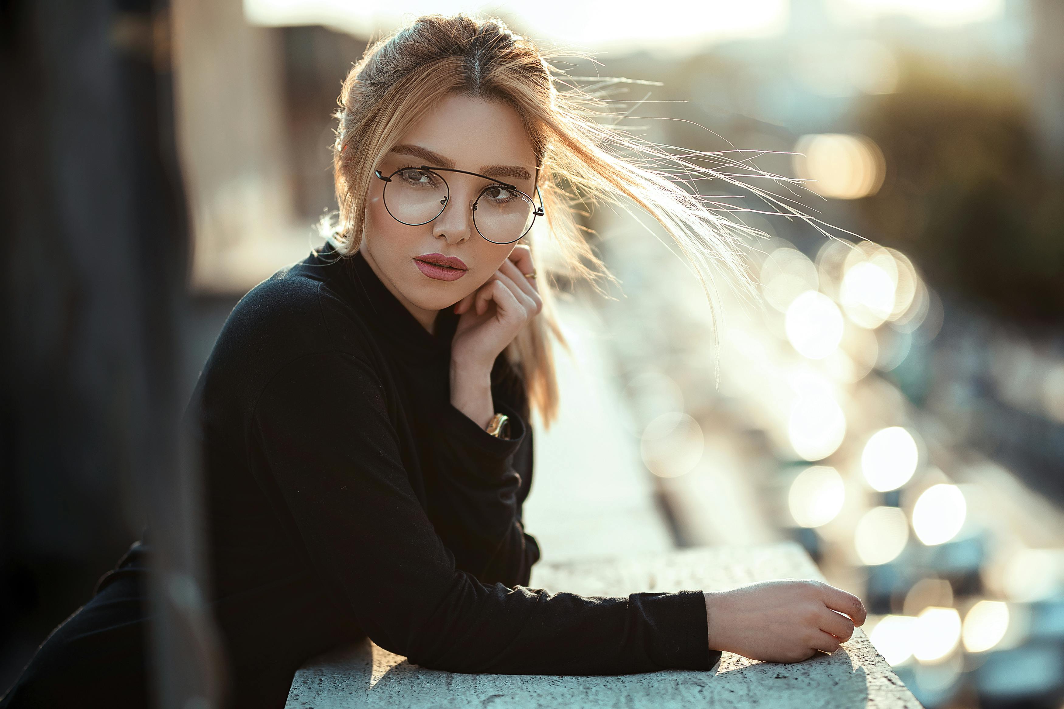 A woman wearing glasses posing leaning on a wall