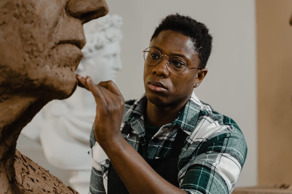 A man wearing glasses sculpting clay